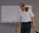 photo of Rainer speaking at a meeting wearing an eyepatch and carrying a stuffed frog on his shoulder
